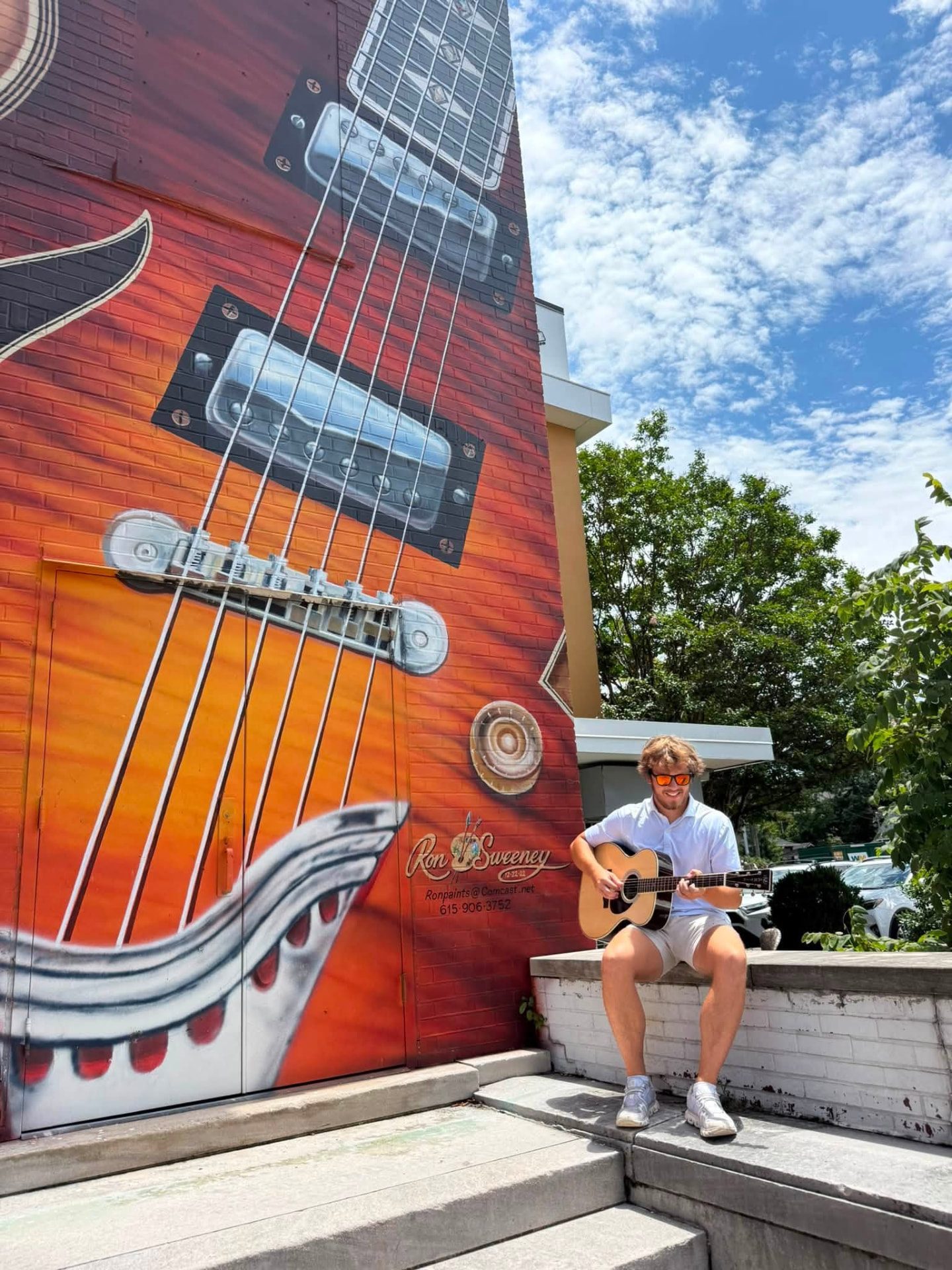 Ethan Maness playing guitar beside a guitar mural
